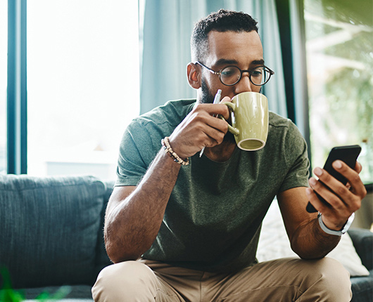 a man with glasses drinking coffee while using a phone